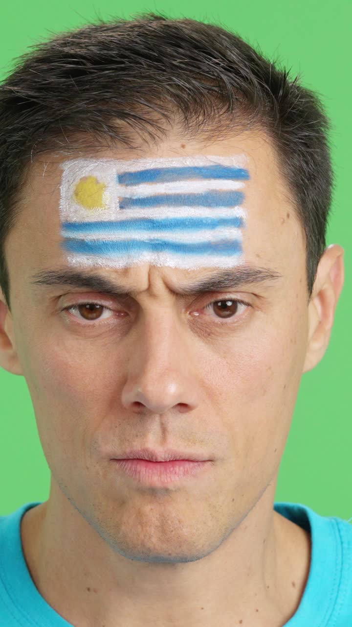 Uomo serio con una bandiera uruguaiana dipinta sul viso