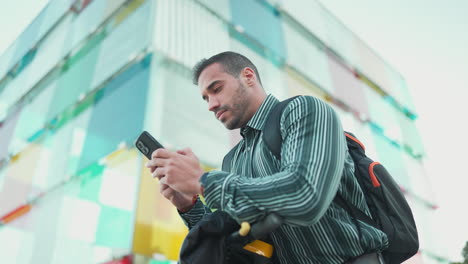 young man checking smartphone while standing in scooter outdoors.