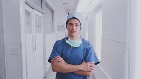 Portrait-Of-Male-Surgeon-Wearing-Scrubs-And-Mask-Standing-In-Hospital-Corridor