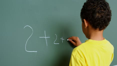 rear view of african american schoolboy solving math problem on chalkboard in classroom at school 4k