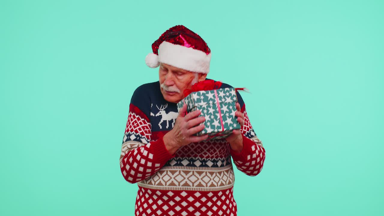Senior grandfather man in christmas sweater received present interested in what inside gift box