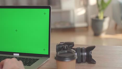 photographer, videographer works on his laptop computer with green screen display