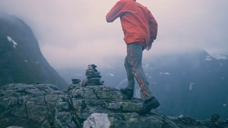man in red jacket running up a hill, towards rocks, reaching his goal and standing still, enjoying the moment. camera pans aroud the man.