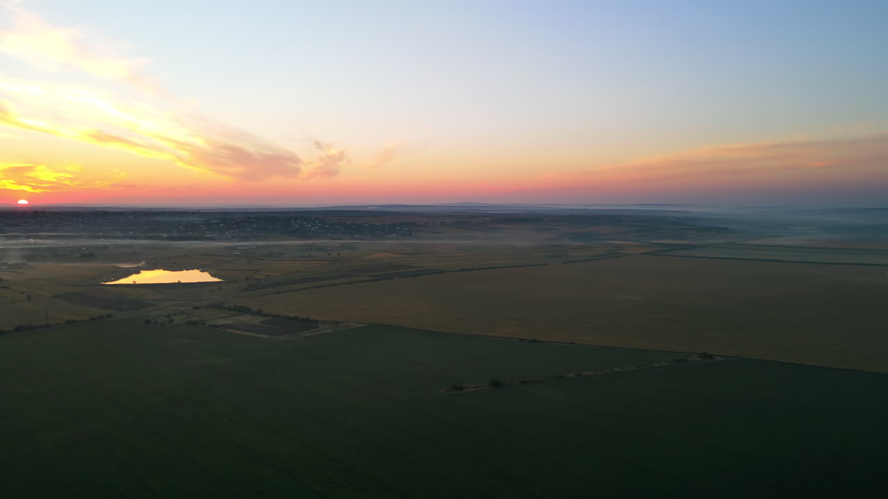 Aerial drone view of village in Moldova at sunset. Few columns of smoke from fires, wide fields, fog in the air