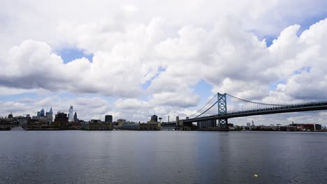 Dunkle-Skyline-Von-Philadelphia-Mit-Wolken-über-Dem-Ruhigen-Delaware-River-Mit-Der-Benjamin-Franklin-Bridge-An-Einem-Warmen-Tag-Mit-Niedrigem-Wasserstand