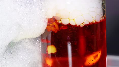 un líquido rojo vibrante reacciona con hielo seco, creando espuma burbujeante en un frasco de vidrio, mostrando una reacción química dinámica