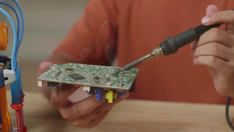 un primer plano de la mano de un niño asiático sosteniendo y arreglando la placa de circuitos mientras repara una mano de cyborg en casa