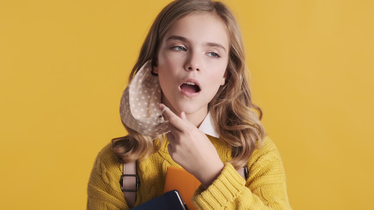 행복한 십대 백인 소녀가 얼굴 마스크를 벗고 책을 들고 있습니다.