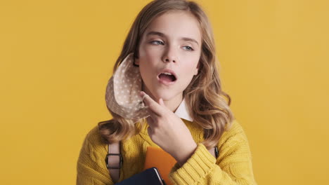 una adolescente caucásica feliz sacando su máscara facial y sosteniendo libros.