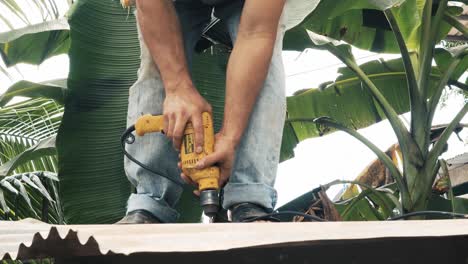 Construction-worker-using-a-pawer-drill-tool-to-screw-through-a-zinc-sheet-into-a-c-purlin-that's-part-of-a-metal-structure-in-a-rural-construction-site