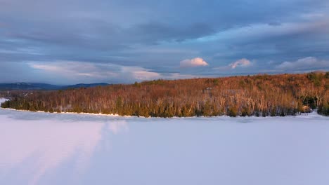 Luftaufnahmen,-Die-Hoch-Und-Nach-Links-Hoch-über-Dem-Zugefrorenen-See-Bei-Sonnenuntergang-Mit-Dunklem,-Stimmungsvollem-Himmel-Und-Goldenem-Licht-Fliegen