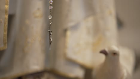 Close-up-of-a-crucifix-pendant-on-a-rosary-with-a-blurred-dove-in-the-background,-symbolizing-peace-and-faith