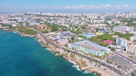 aerial flyover coastline of santo domingo cityscape and traffic on coastal road during sunny day - dominican republic