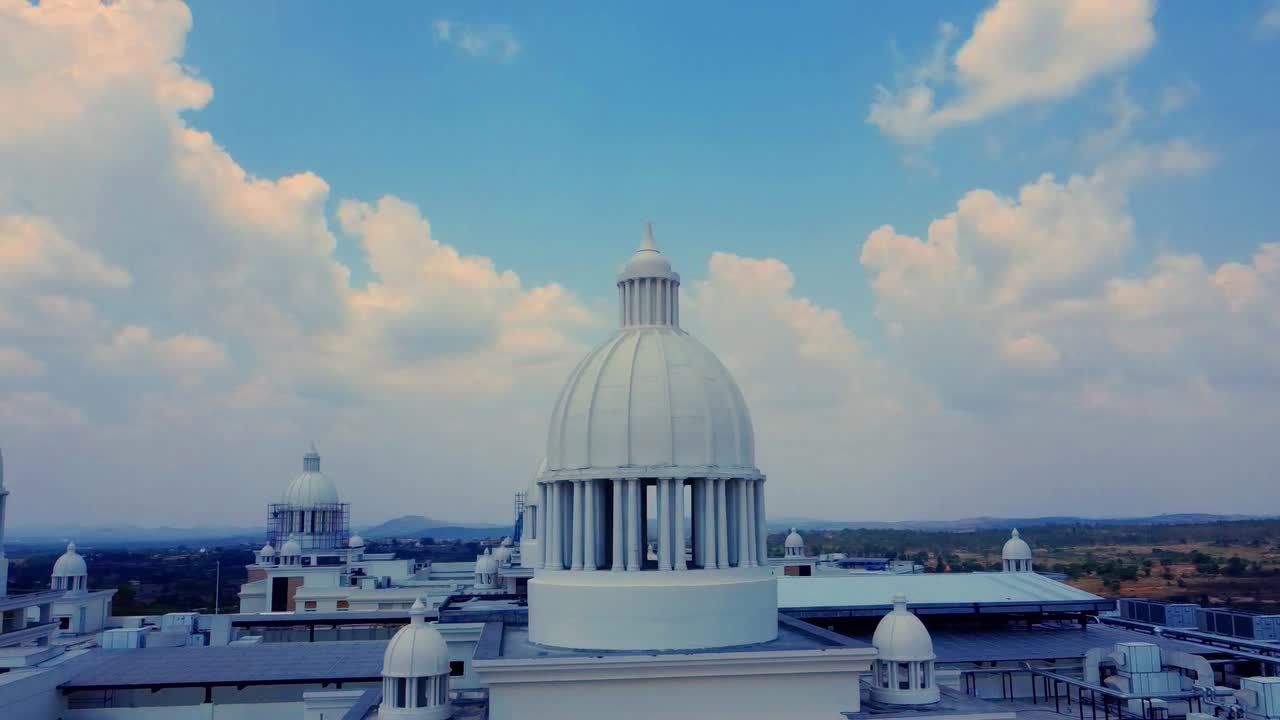 A cinematic aerial shot orbiting the rooftop of a grand neo-classical building, revealing its many majestic white domes against a beautiful blue sky with puffy white clouds, symbolizing success