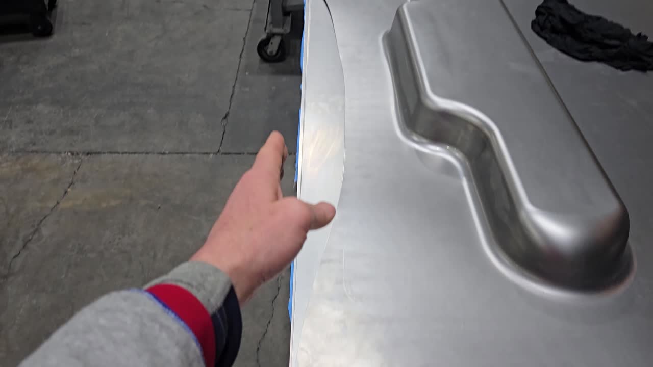 Mano de trabajador señalando una lámina de metal conformada durante el proceso de fabricación de piezas de automóviles.