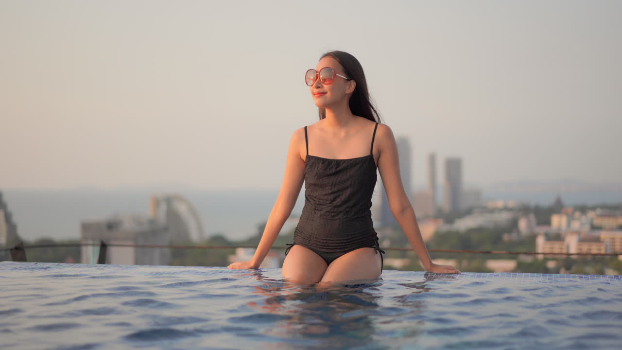 도시 경관을 배경으로 옥상 인피니티 수영장 옆에 앉아 있는 여성