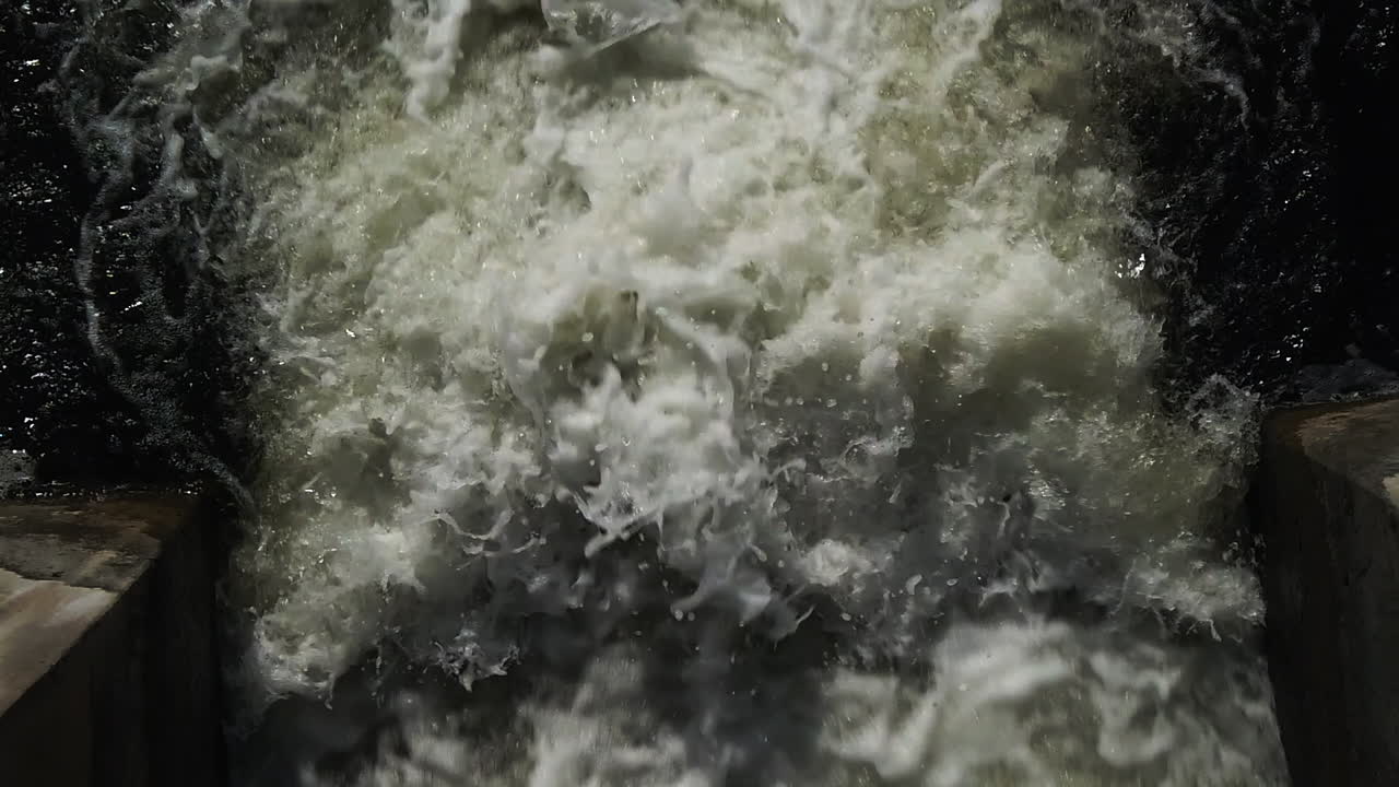 Rapid water erupting downstream out of the Eramosa River sluice gate in slow motion, medium wide shot looking downwards