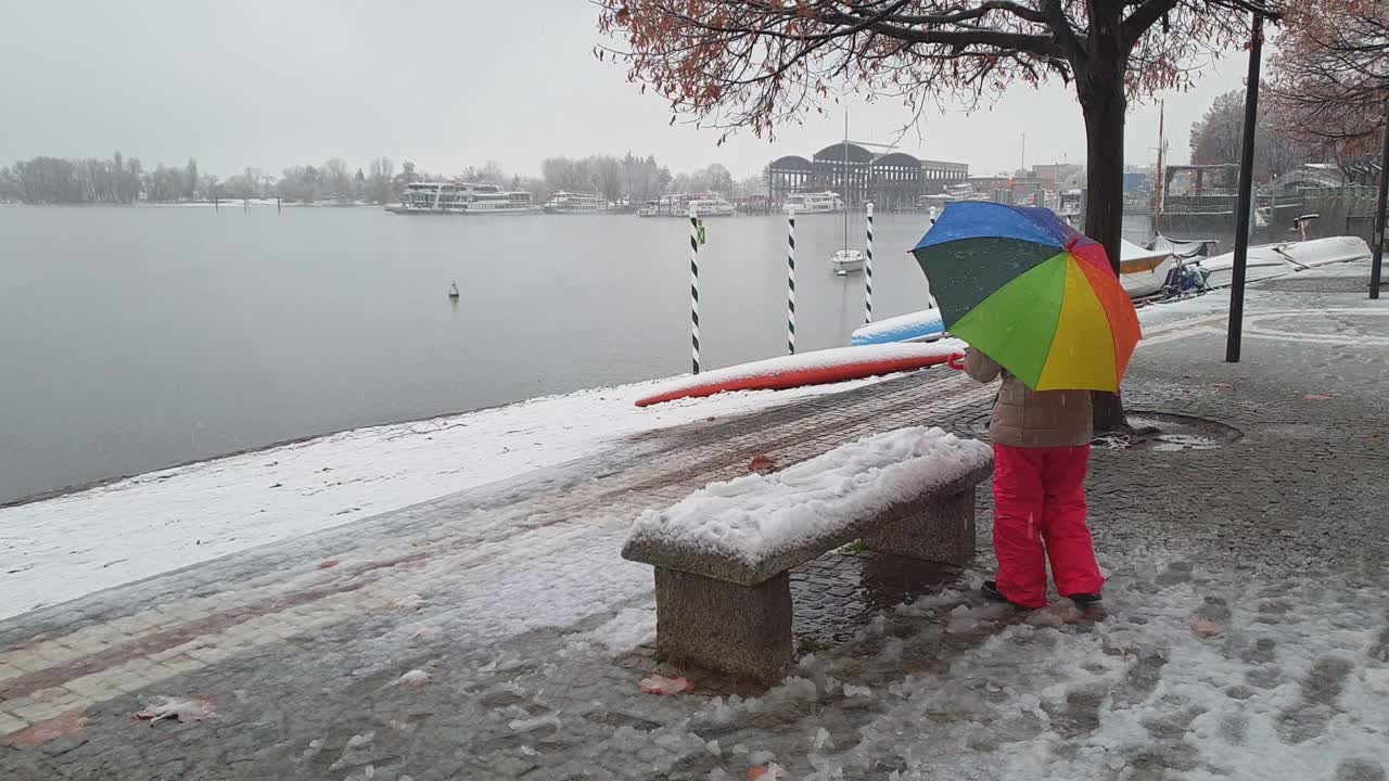 niño sosteniendo hermosos paraguas coloridos juega con nieve en un banco en arona
