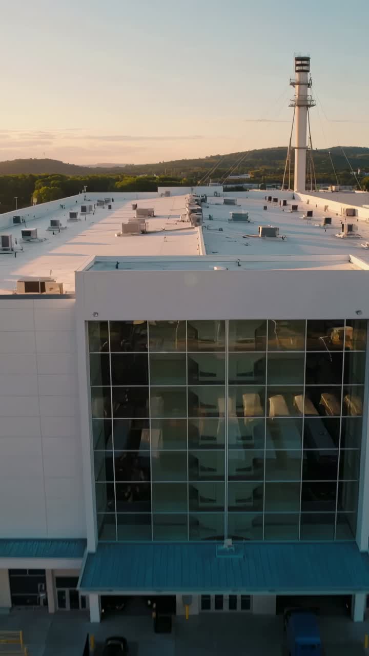 Vídeo vertical: dron retrocediendo, revelando un almacén blanco con muro cortina de cristal y tráileres