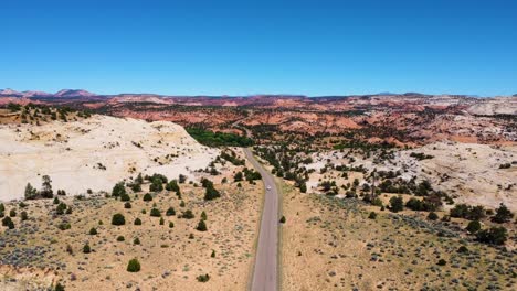 Einzelnes-Weißes-Auto,-Das-In-Der-Wüstenlandschaft-Von-Utah-Auf-Die-Kamera-Zufährt,-Sonnige-Bergautobahnroute-In-Den-USA