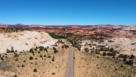 un solo coche blanco conduciendo hacia la cámara en el paisaje del desierto de utah, carretera de montaña soleada en ee.uu.