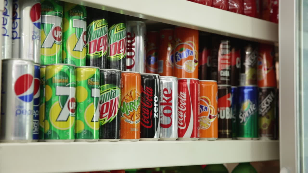 Various soda cans displayed on supermarket shelf in vibrant packaging, ready for selection