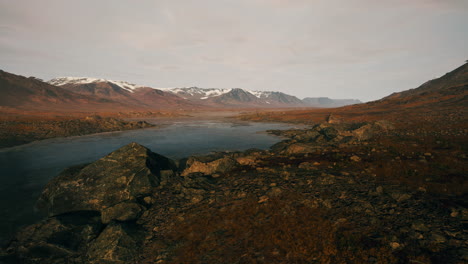 Clear-river-with-rocks-leads-towards-mountains-lit-by-sunset