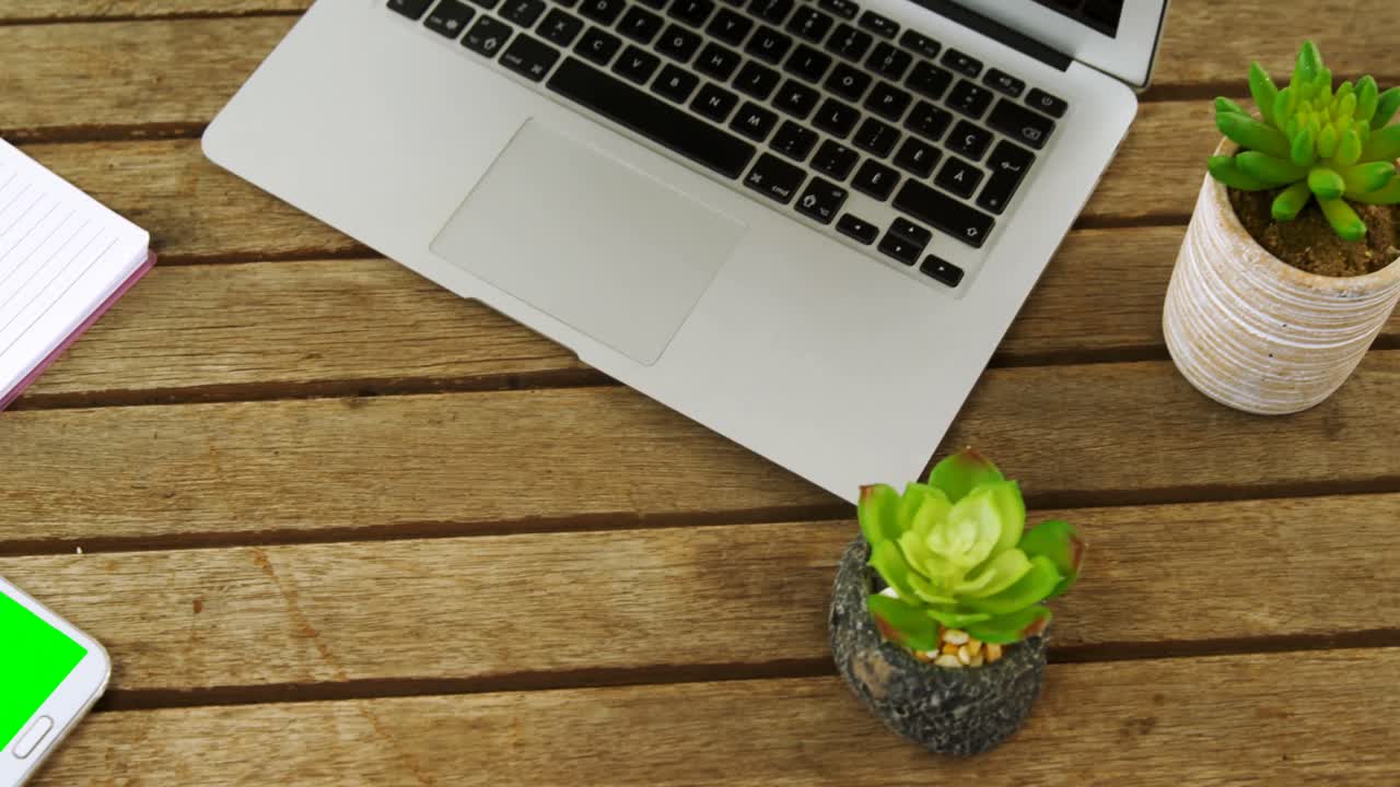 Laptop, pot plant, mobile phone, pen and notepad on table 4k