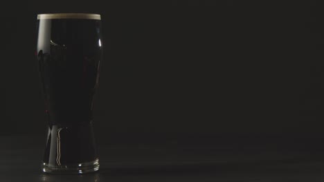 pinta de cerveza negra irlandesa en vidrio contra el fondo negro del estudio para celebrar el día 1 de san patricio