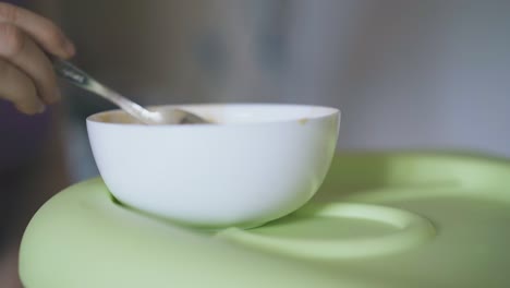 woman takes cream soup from white bowl to feed baby at table