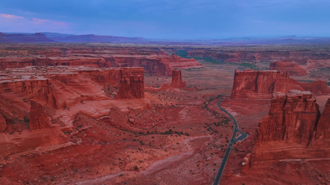 Stort, øde landskap med rød jord og steiner. En motorvei krysser området. Droneflygning over canyonene i Arches nasjonalpark, Utah, USA