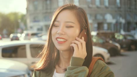 즐거운 젊고 예쁜 소녀가 전화로 이야기하고 시끄러운 거리에서 웃고 있습니다.