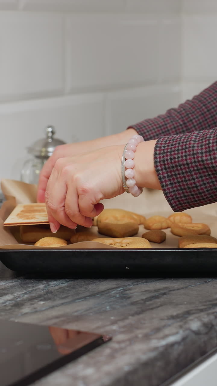 леди осторожно помещает свежевыпеченное печенье на пергаментную бумагу, используя мультфильм для сушки лишнего масла, в окружении кухонной посуды и ингредиентов, таких как печенье и красочные начинки