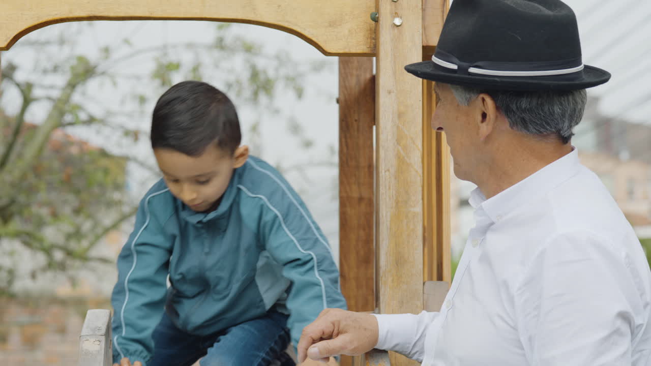 A tender moment between grandfather and grandson as they play together in a wooden playhouse with a slide in the backyard.