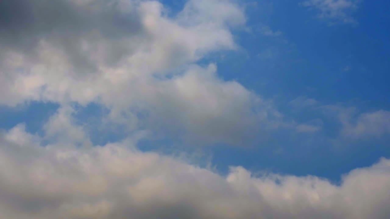 Soft white clouds drift across a bright blue sky on a warm and breezy afternoon