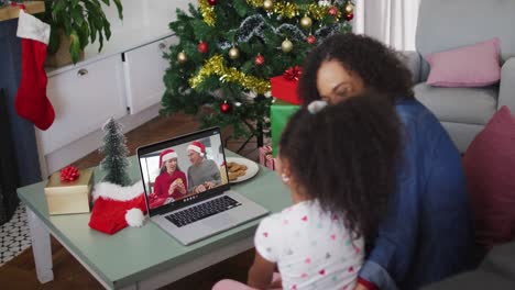 Happy-african-american-mother-and-daughter-on-video-call-on-laptop-with-friends-at-christmas