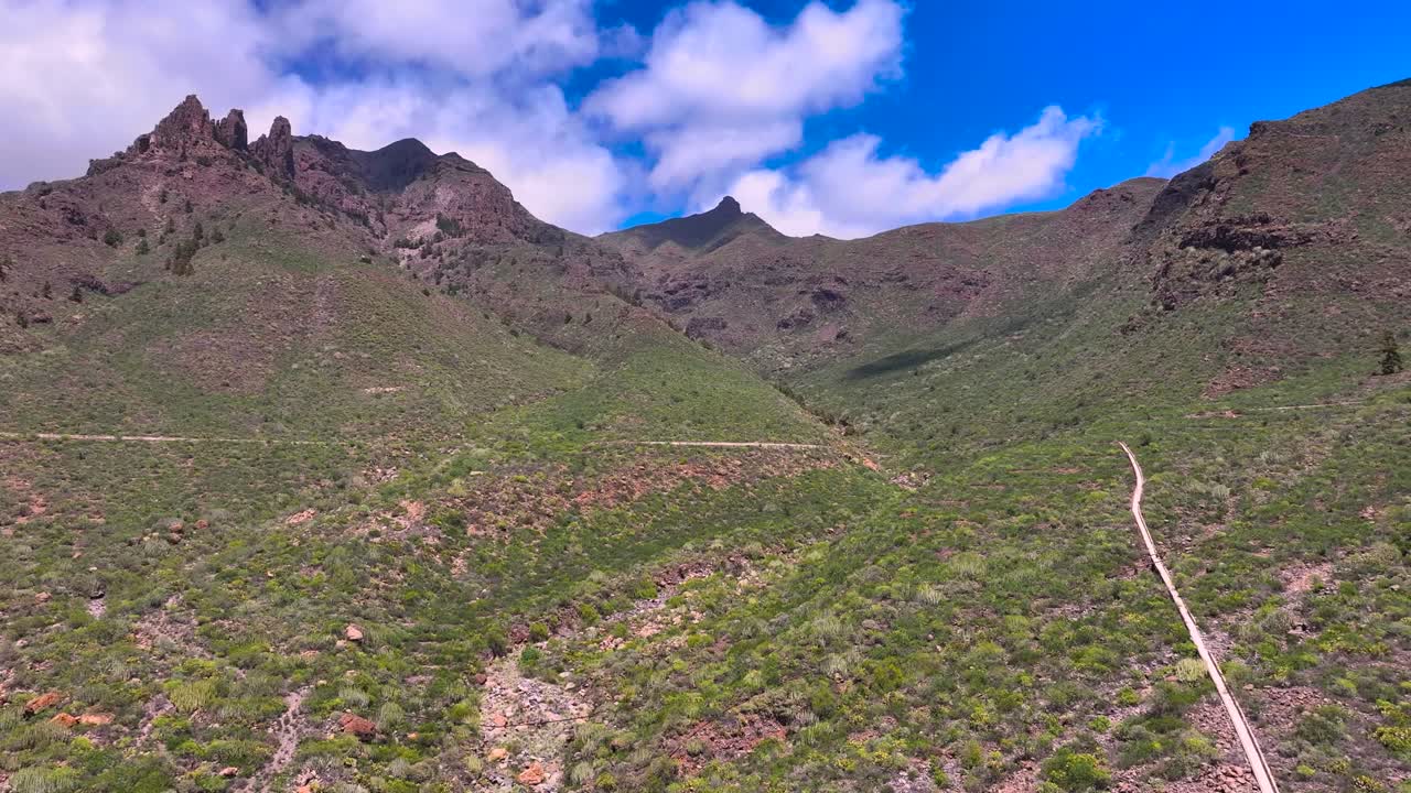 Volcanic mountain terrain with green slopes and a narrow irrigation ditch path