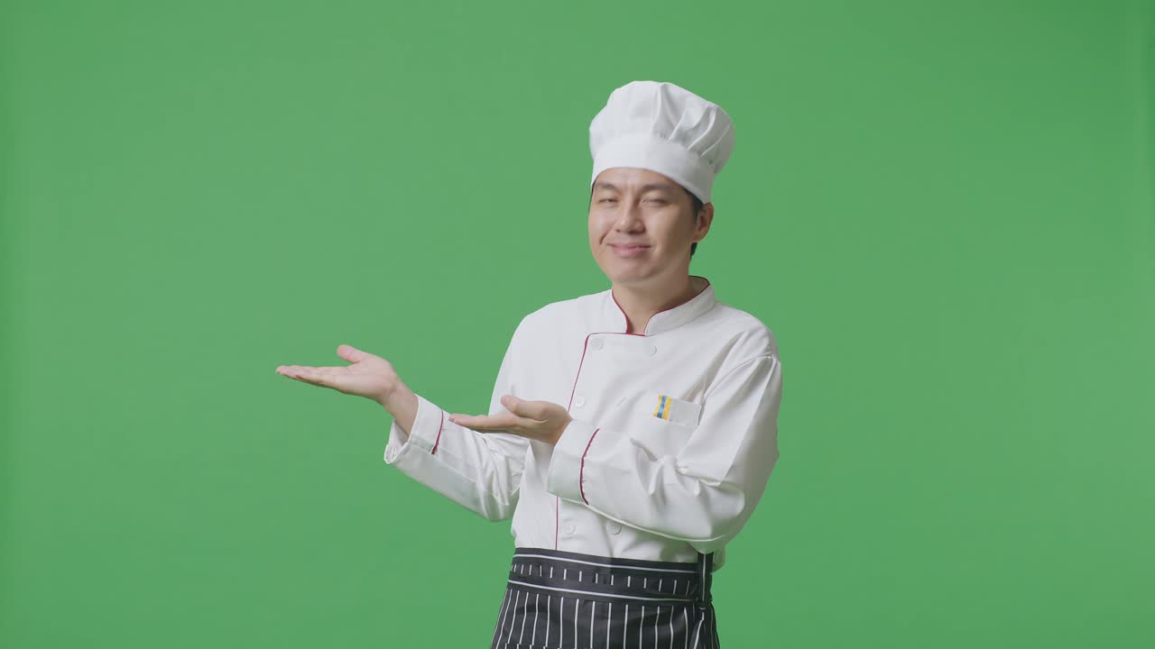 녹색 스크린 배경 스튜디오에 서 있는 아시아 남자 셰프가 미소 짓고 을 가리키고 있다