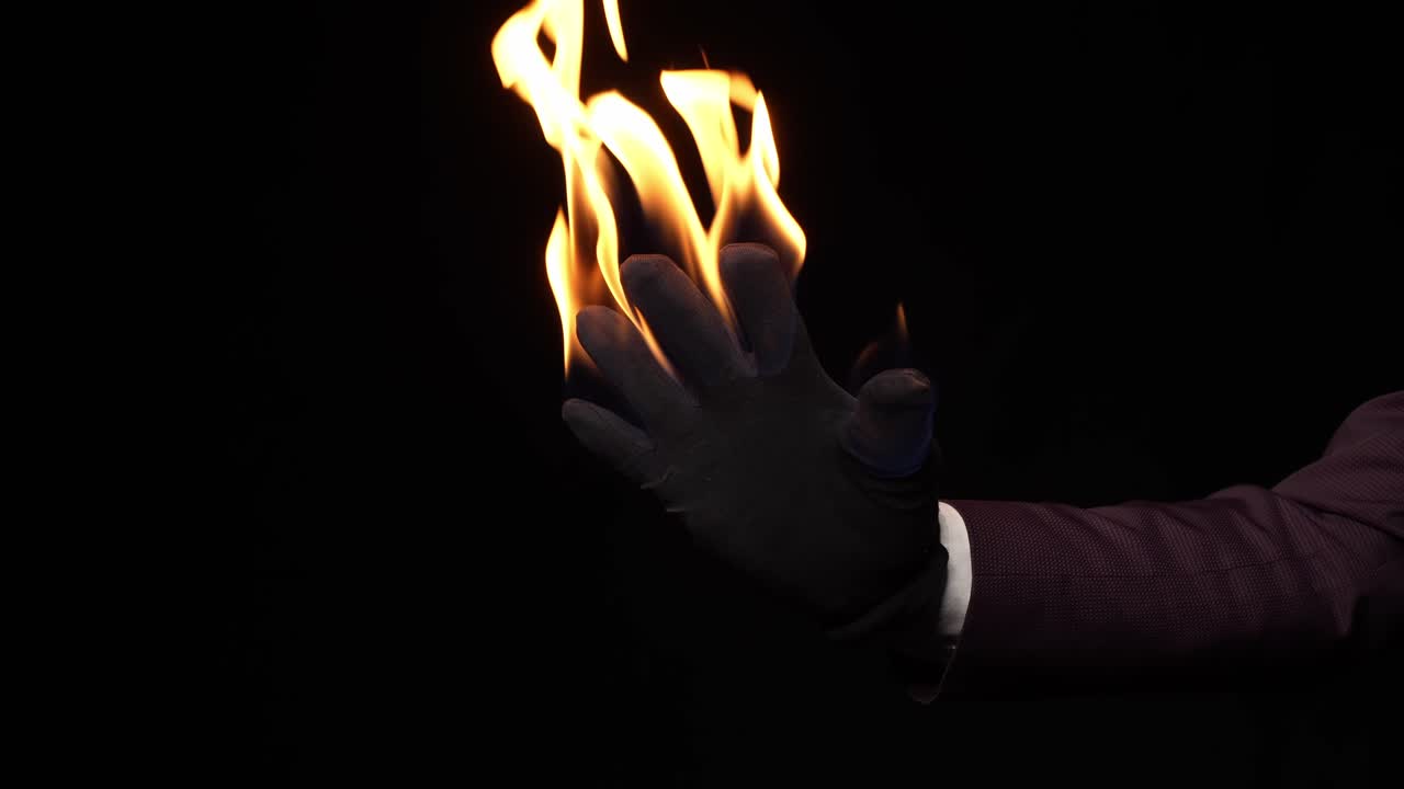 Gloved Hand With Burning Flame Against Dark Background. Illusionist's Fire. closeup shot