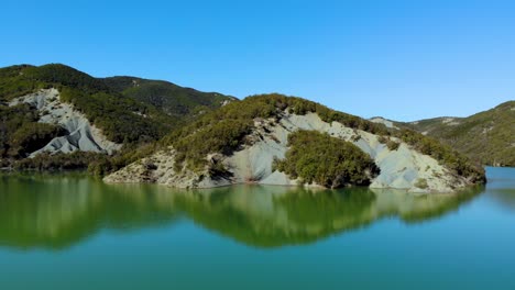 paradise mountain lake with calm clear water reflecting lush vegetation and bright blue sky on a sunny day in alps