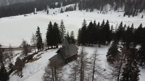 Drone-De-Vértigo-De-Una-Antigua-Iglesia-De-Piedra-Y-Madera-En-Un-Bosque-Invernal-Que-Muestra-Un-Lago-Congelado-Detrás-De-Ella