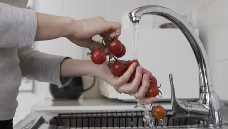 close sideways shot washing cherry tomatoes with running tap water at the sink in the kitchen