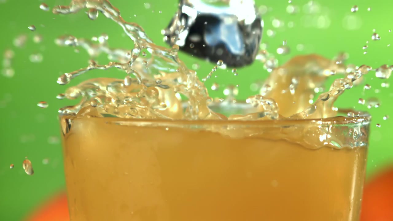 Slow Motion Ice Cubes Splashing into a Glass of Orange Juice