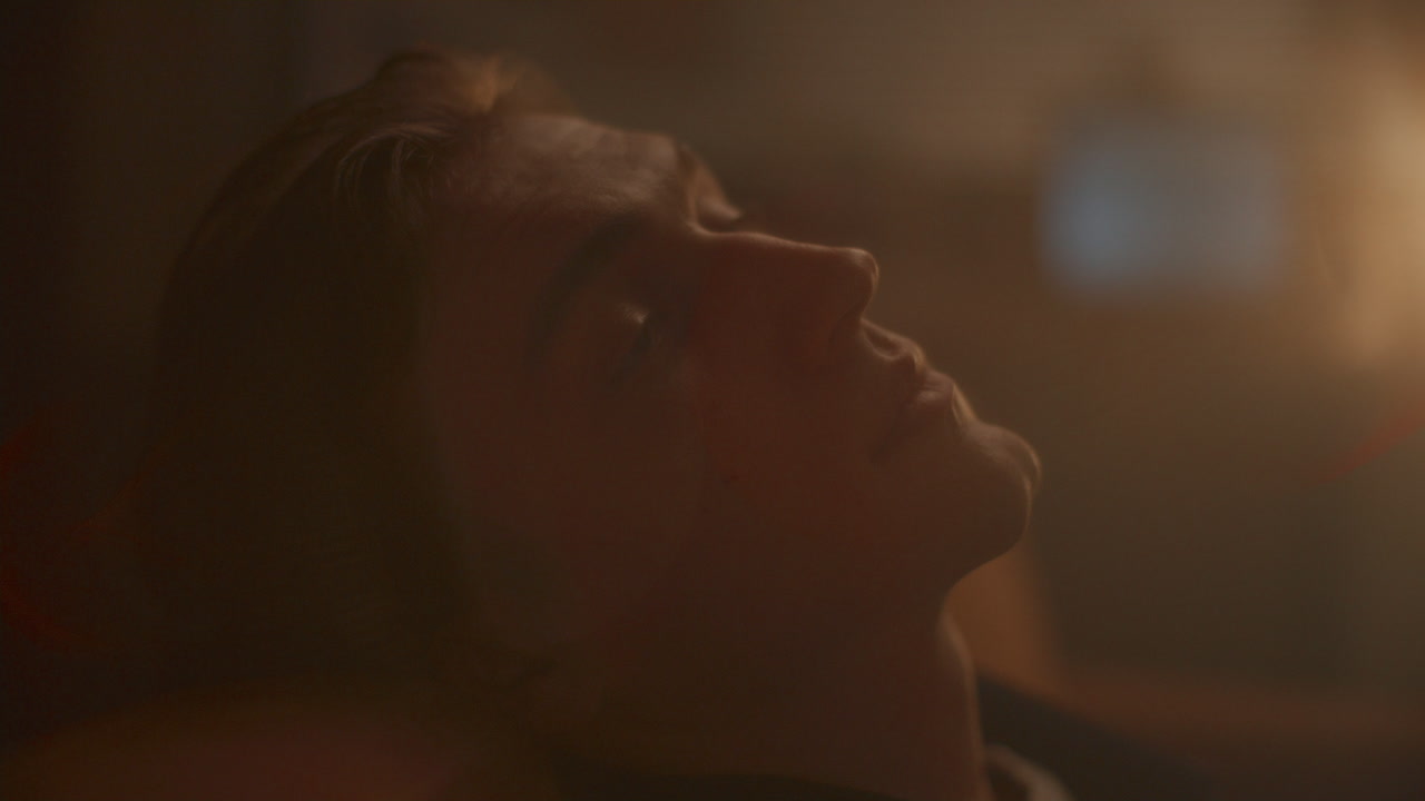 Young Pensive Man Reclining on Sofa with Reflective Expression in Dimly Lit Room