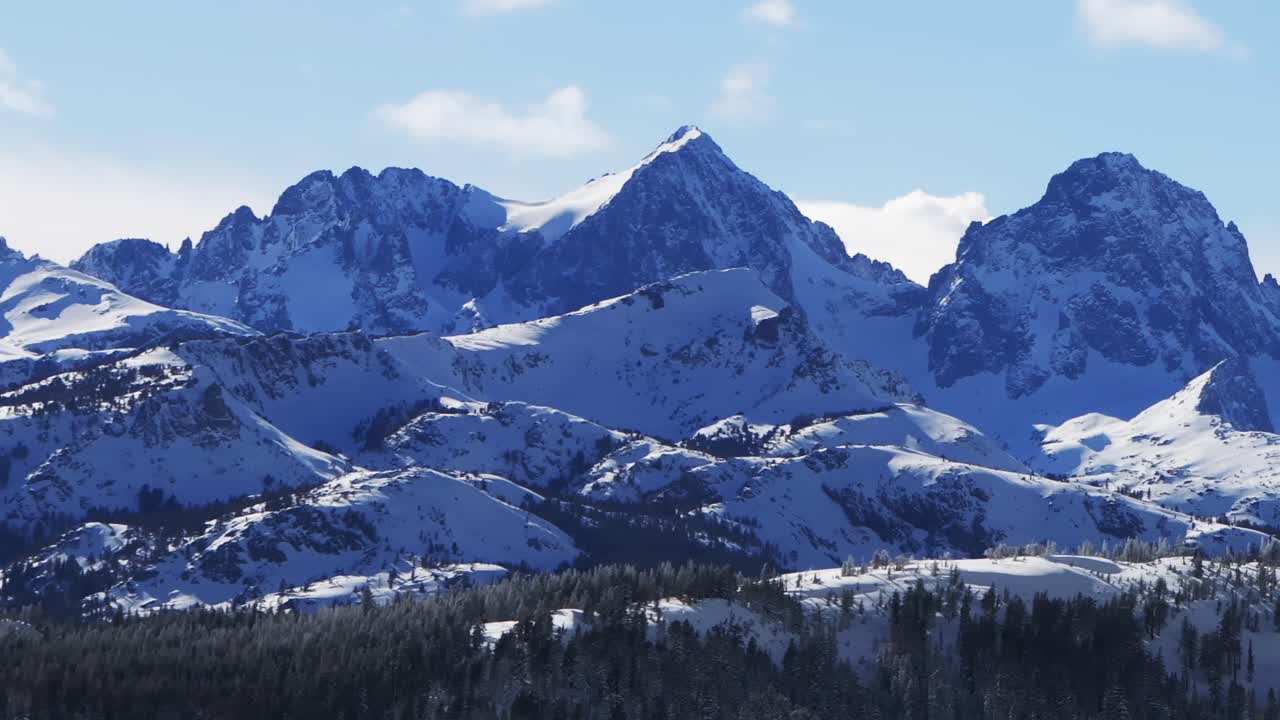 Das Ski- und Snowboardresort The Hemlocks Mammoth Mountain, sonniger Winternachmittag mit blauem Himmel, Drohnenaufnahme Kalifornien, die zerklüfteten, aufragenden Gipfel der Minarets, frischer Tiefschnee, Wolken, Landschaft des Inyo National Forest, Zoom