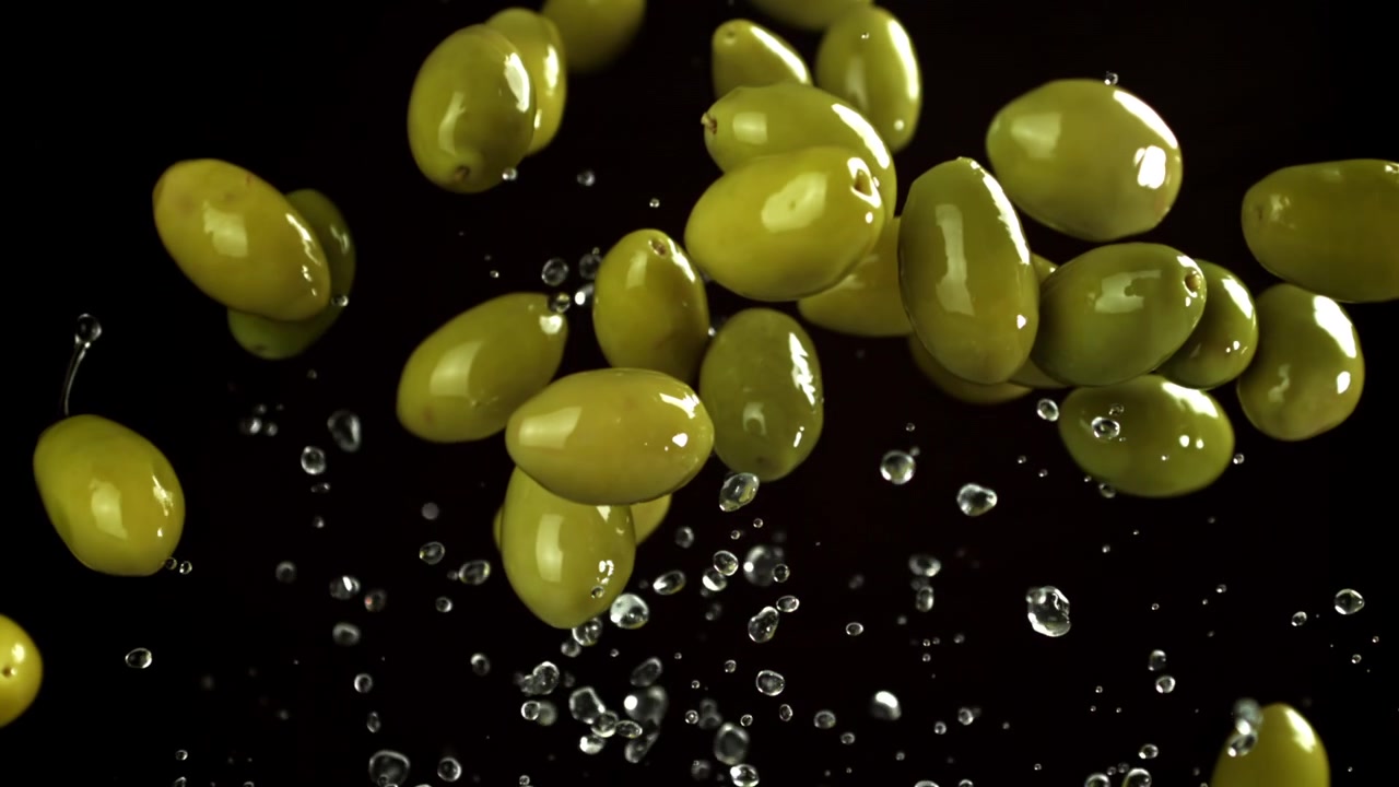 Movimento super rallentato di olive verdi che cadono con gocce d'acqua.