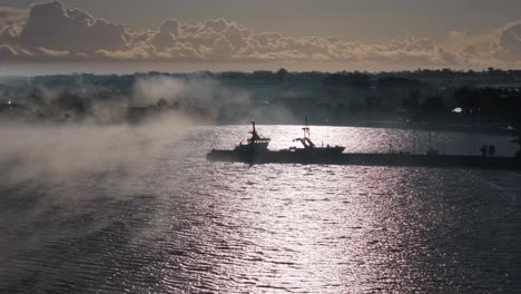 a fishing boat on calm waters with mist rising at sunrise in carlingford marina, ireland