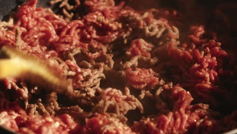 process of cooking ground meat in a pan, stirred with a wooden spatula