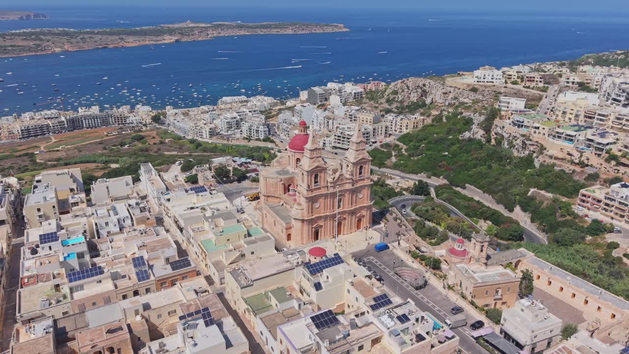 Drone footage of the Mellieha Parish Church with its iconic red dome and twin bell towers, overlooking the Mediterranean Sea in Malta. Fly around the tower