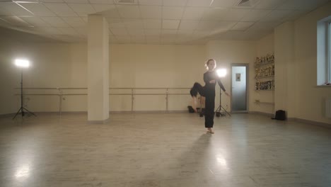 un grupo de jóvenes estudiantes de ballet con ropa de baile negra practicando posiciones en un amplio estudio de ballet con pisos de madera y barras montadas en la pared. expresiones enfocadas y movimientos sincronizados.